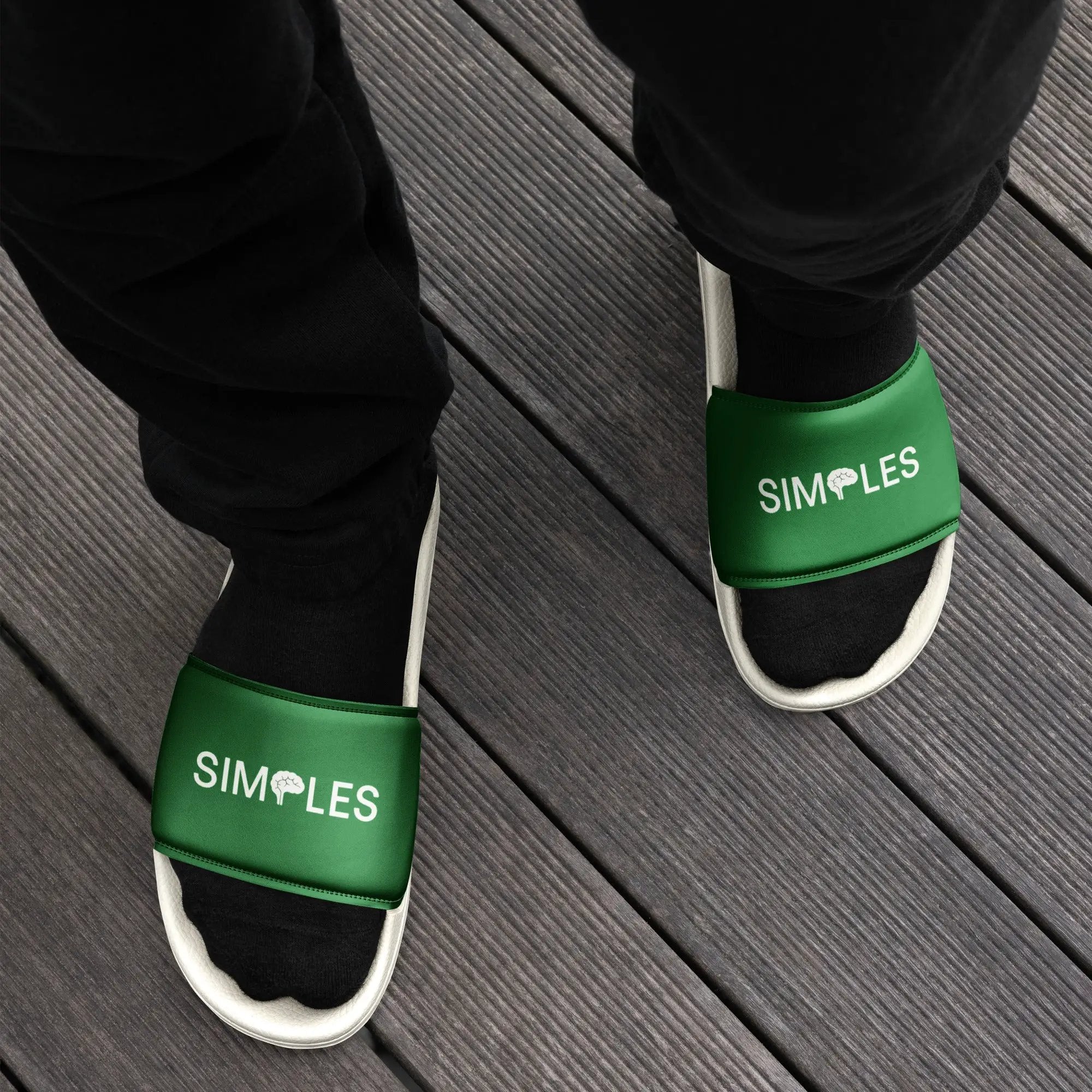 Pair of Men’s Slides by Simples Market, green strap sandals on black pants over a wooden deck.