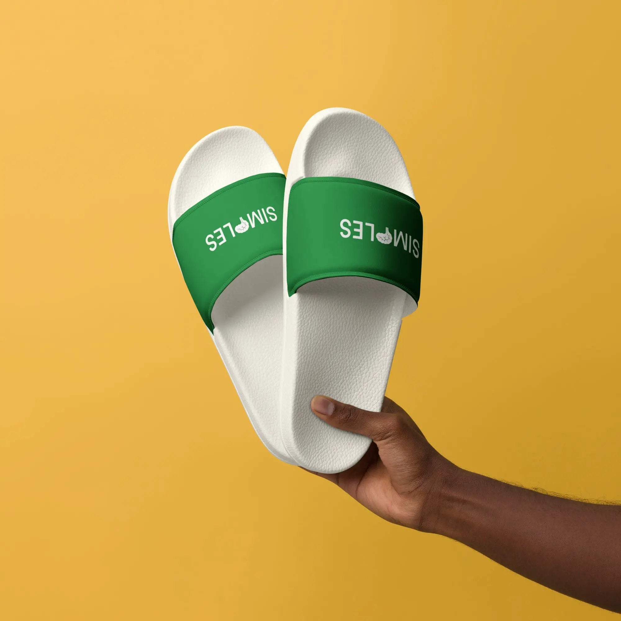 Men’s slides by Simples Market; green strap with white textured sole, hand-held against a yellow background