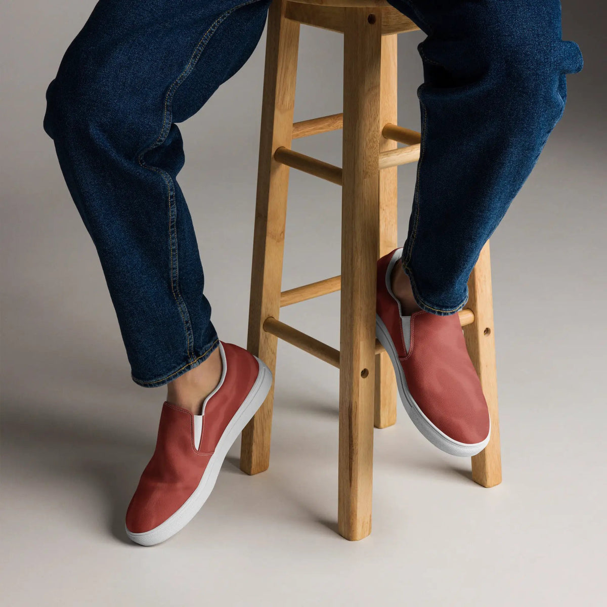 Men's red canvas slip-on shoes on denim jeans, studio shot