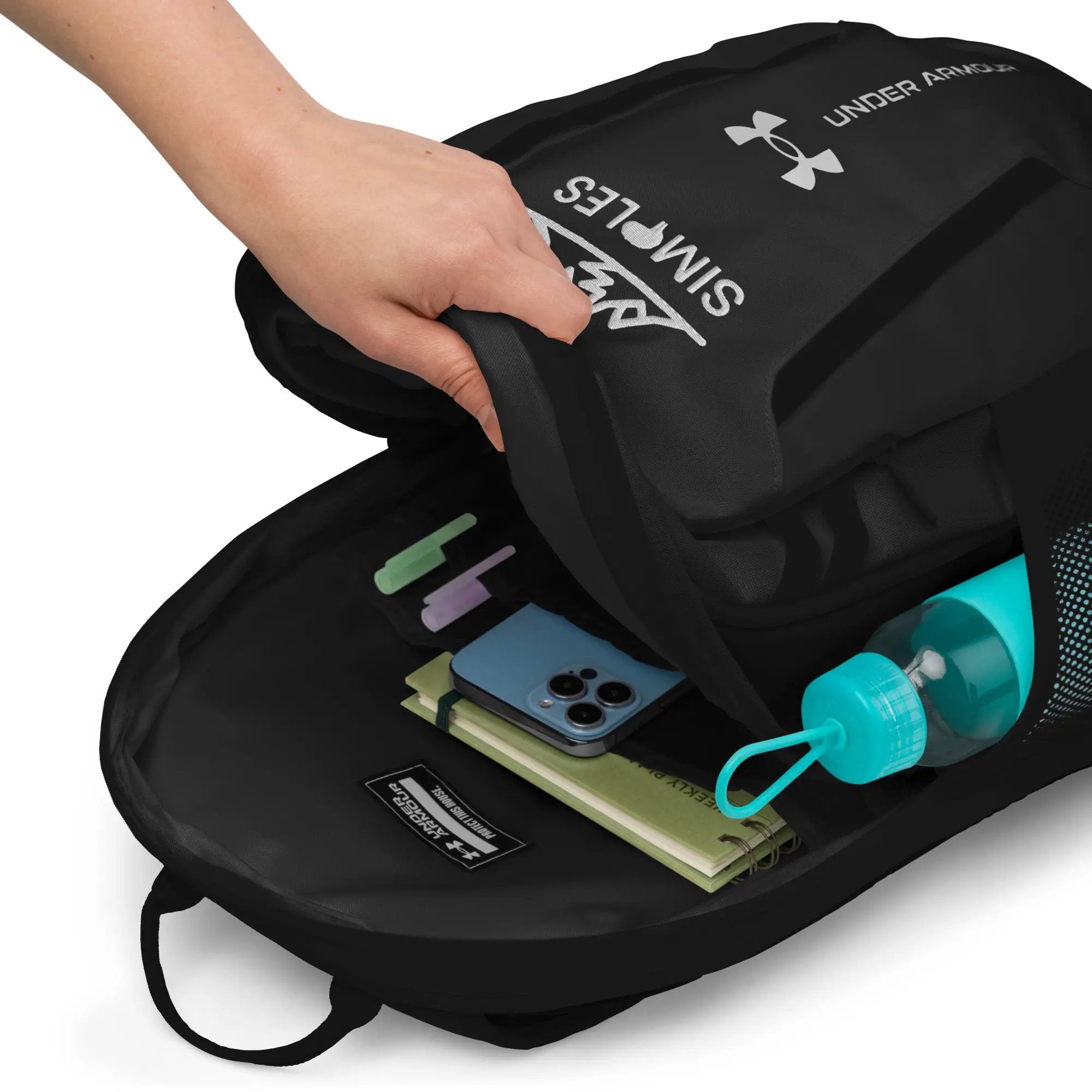 Under Armour backpack, black with logo; open to show notebook, smartphone, water bottle and sticky notes.