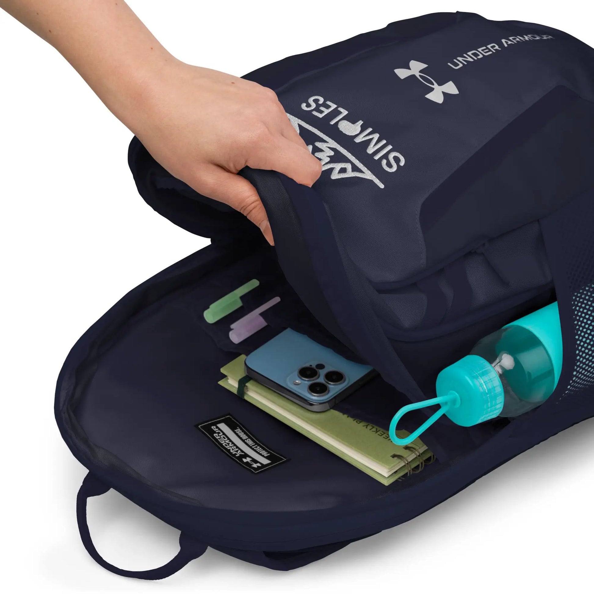 Under Armour backpack in navy blue; open main compartment with notebook, smartphone and water bottle